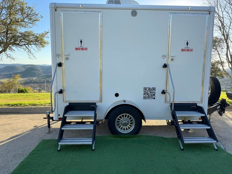 White trailer with two side doors and stair ramps parked beside a road with a scenic landscape view