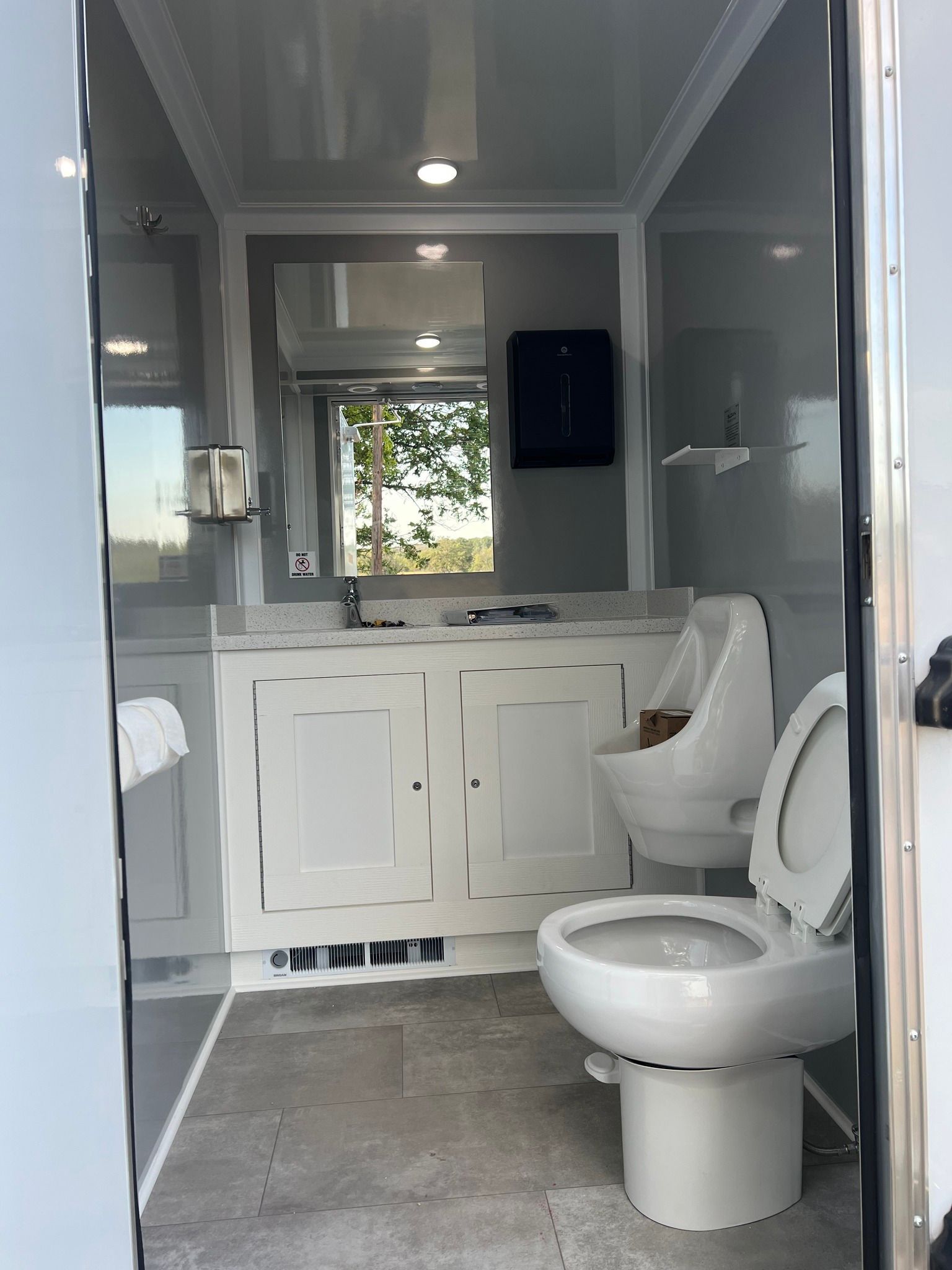 Modern gray bathroom with a toilet, vanity, mirror, shower, and window under the sink.