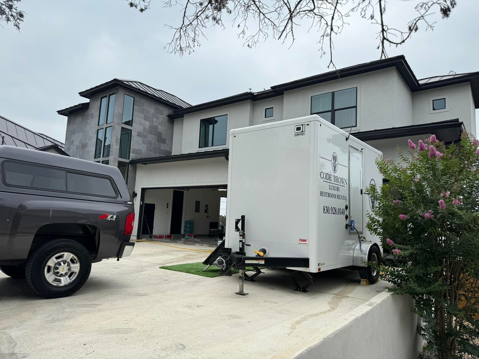 White trailer parked in a driveway beside a black pickup truck in front of a two-story house.