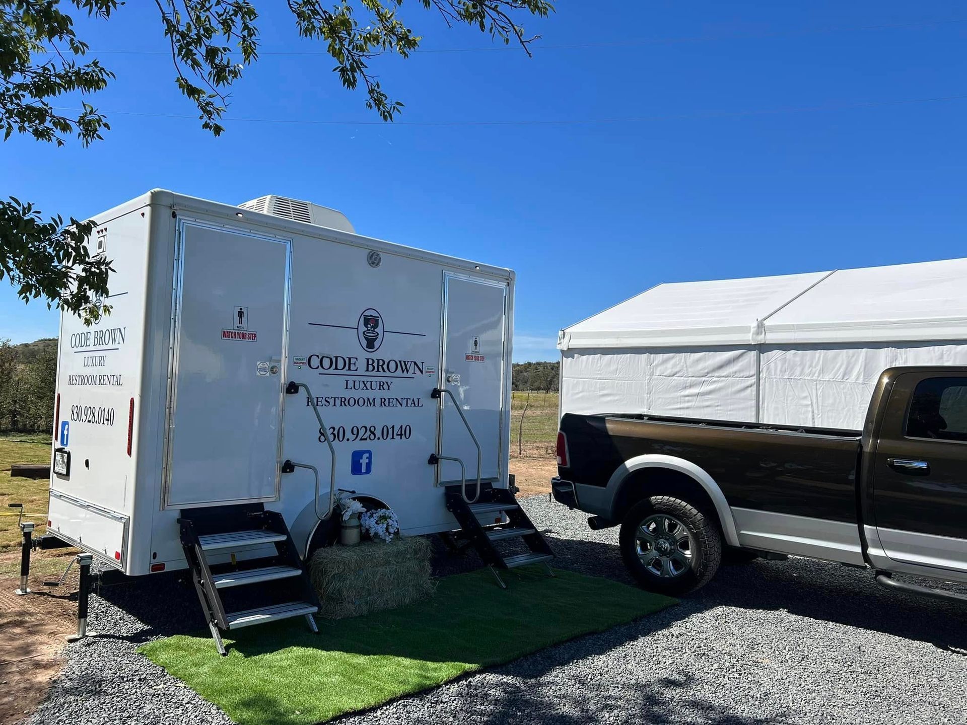 White trailer with steps parked beside a black pickup truck under a clear blue sky.
