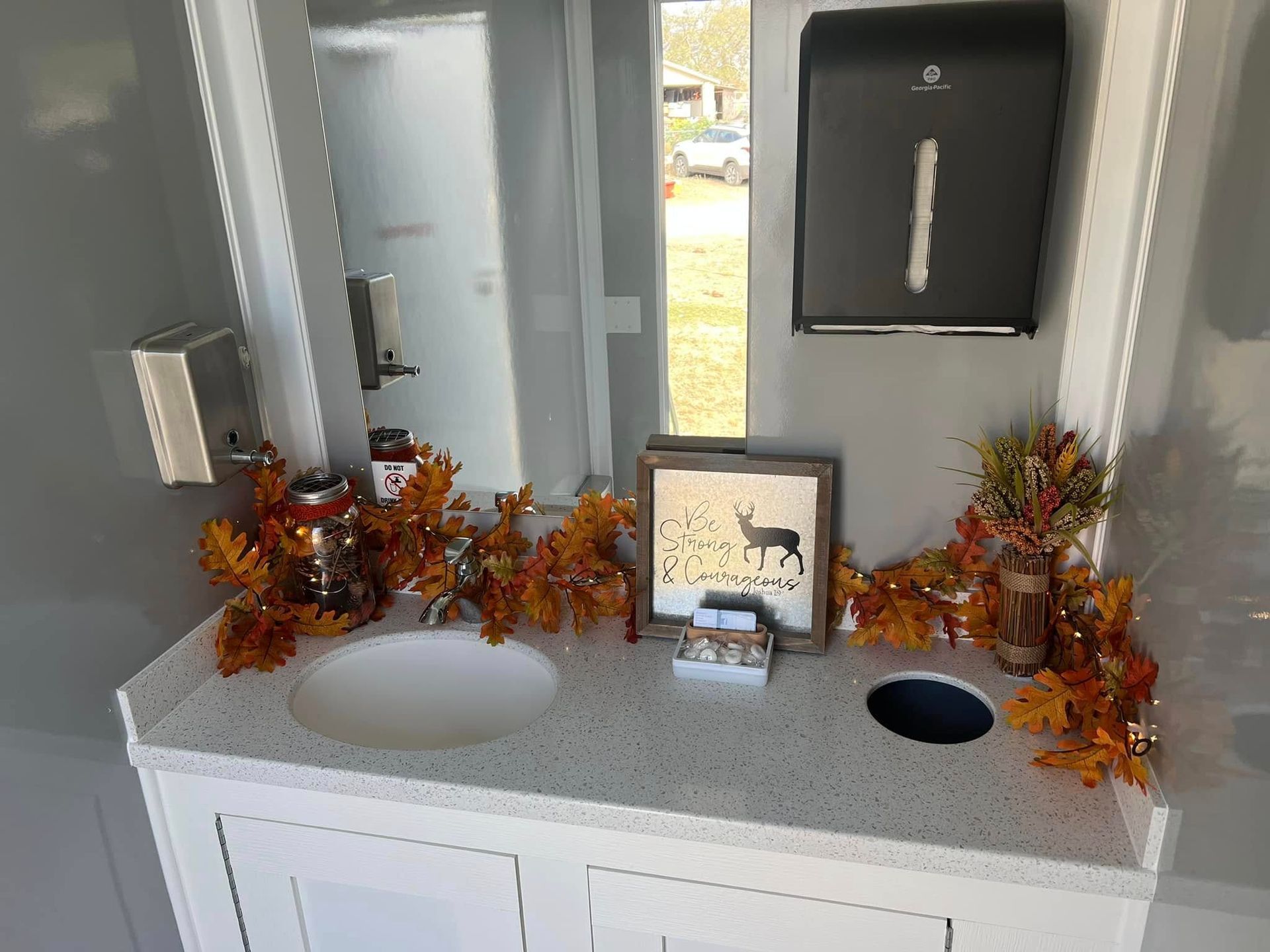Bathroom vanity with white countertop, mirrors, autumn decorations, and sink openings for a future installation