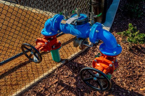 A Blue Pipe With Two Red Valves Attached To It Is Sitting Next To A Chain Link Fence - Fulton, CA - Devoto Plumbing, Inc.