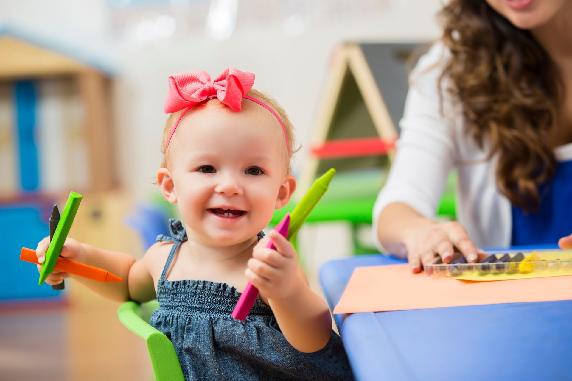 A baby girl is sitting at a table holding a crayon.