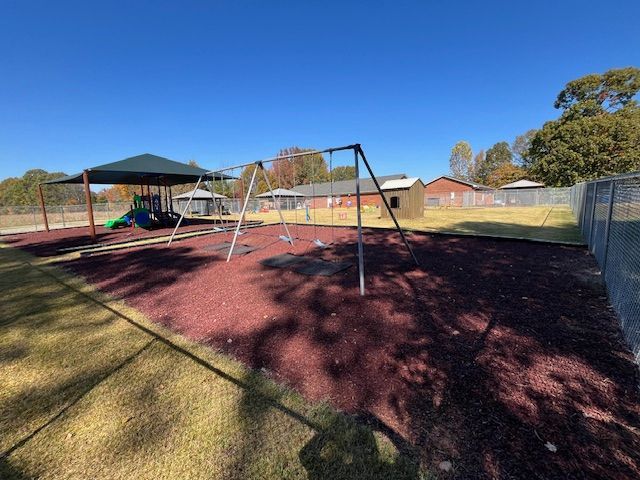 A playground with swings , a covered area and a fence.