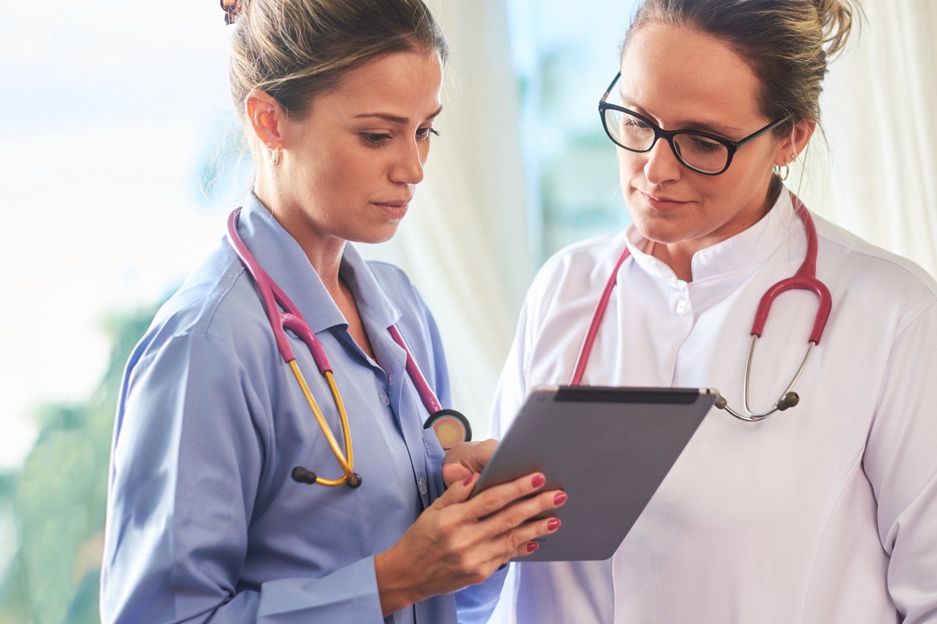 Two female doctors are looking at a tablet together.