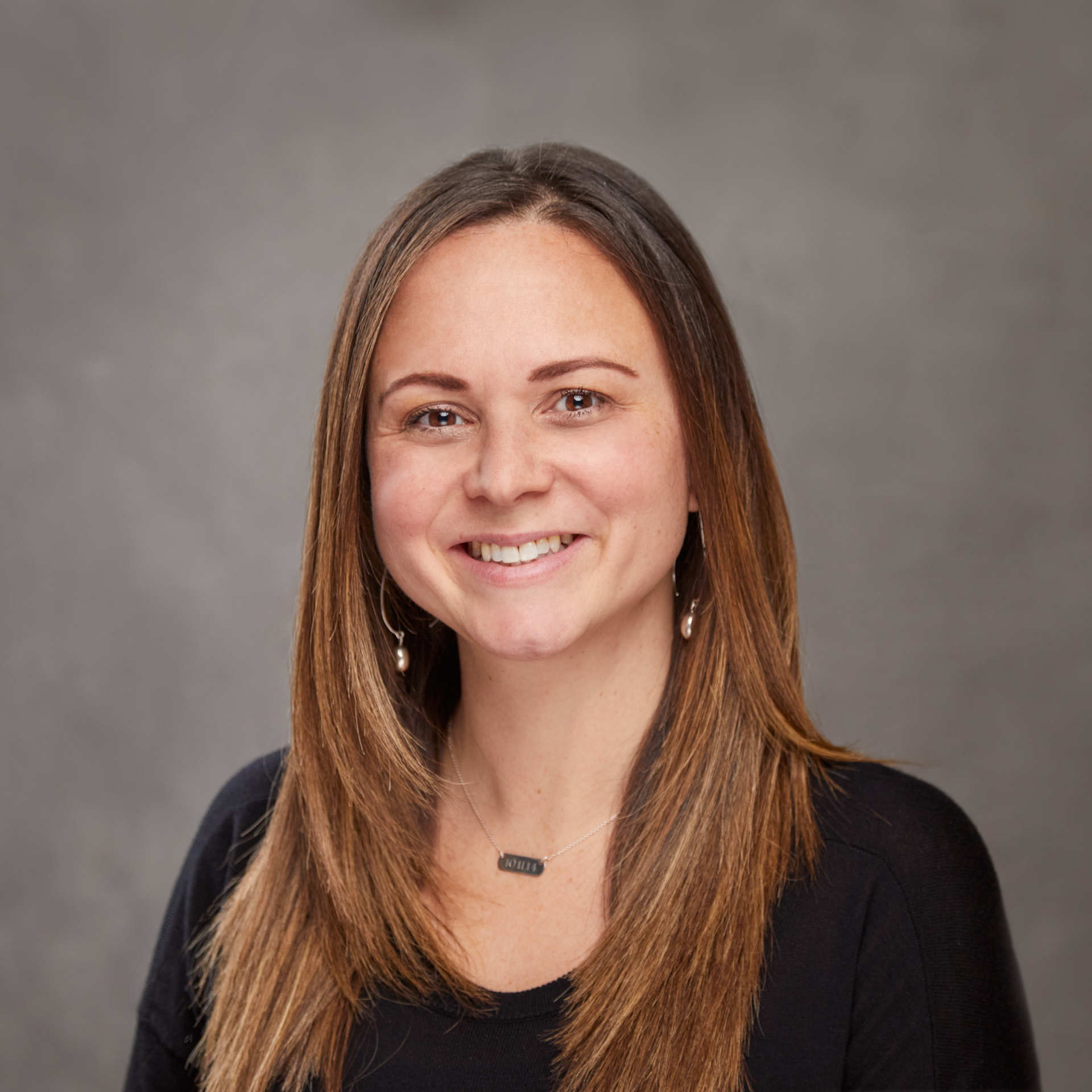 A woman wearing a black shirt and earrings is smiling for the camera.