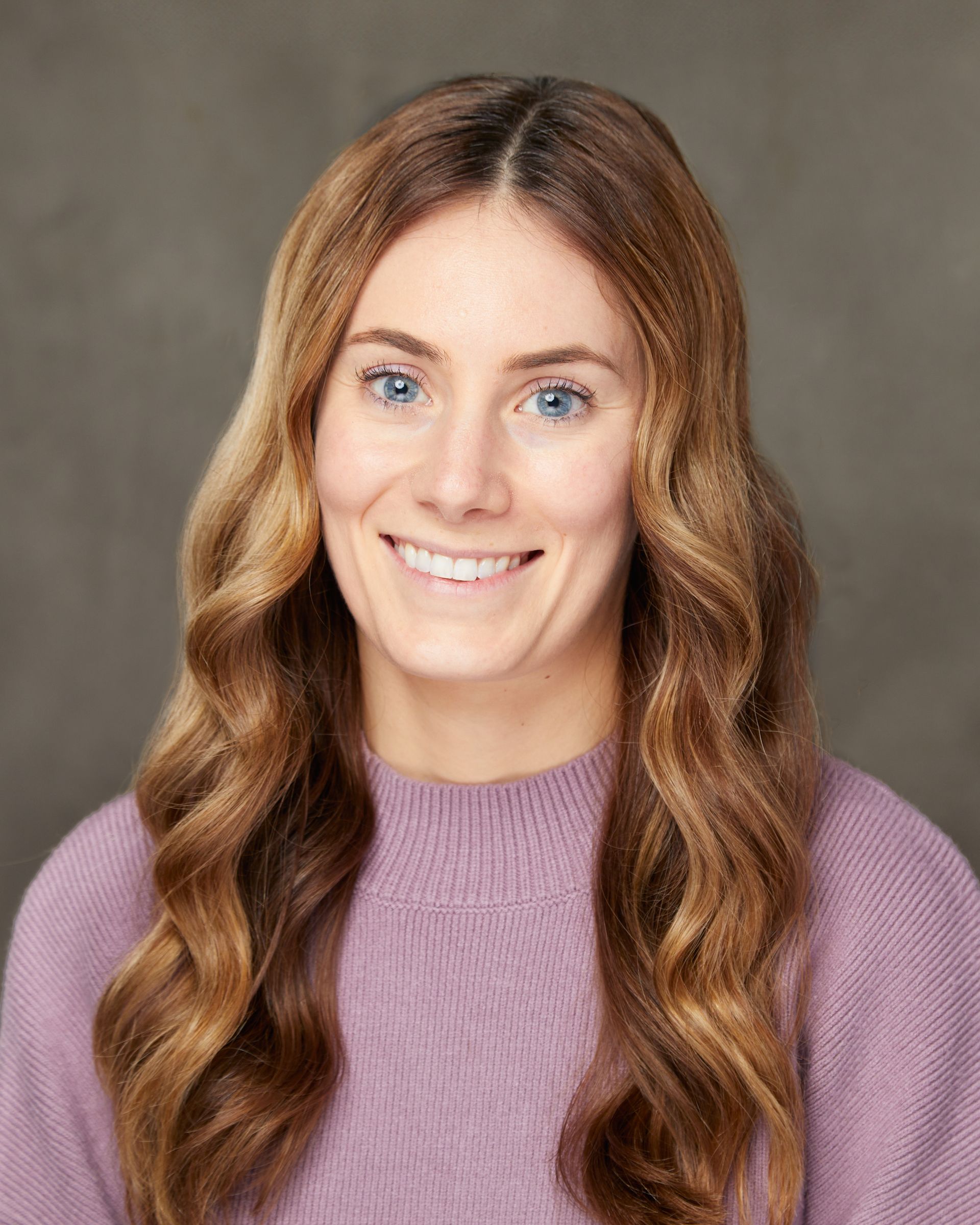 The woman is wearing a purple sweater and smiling for the camera.