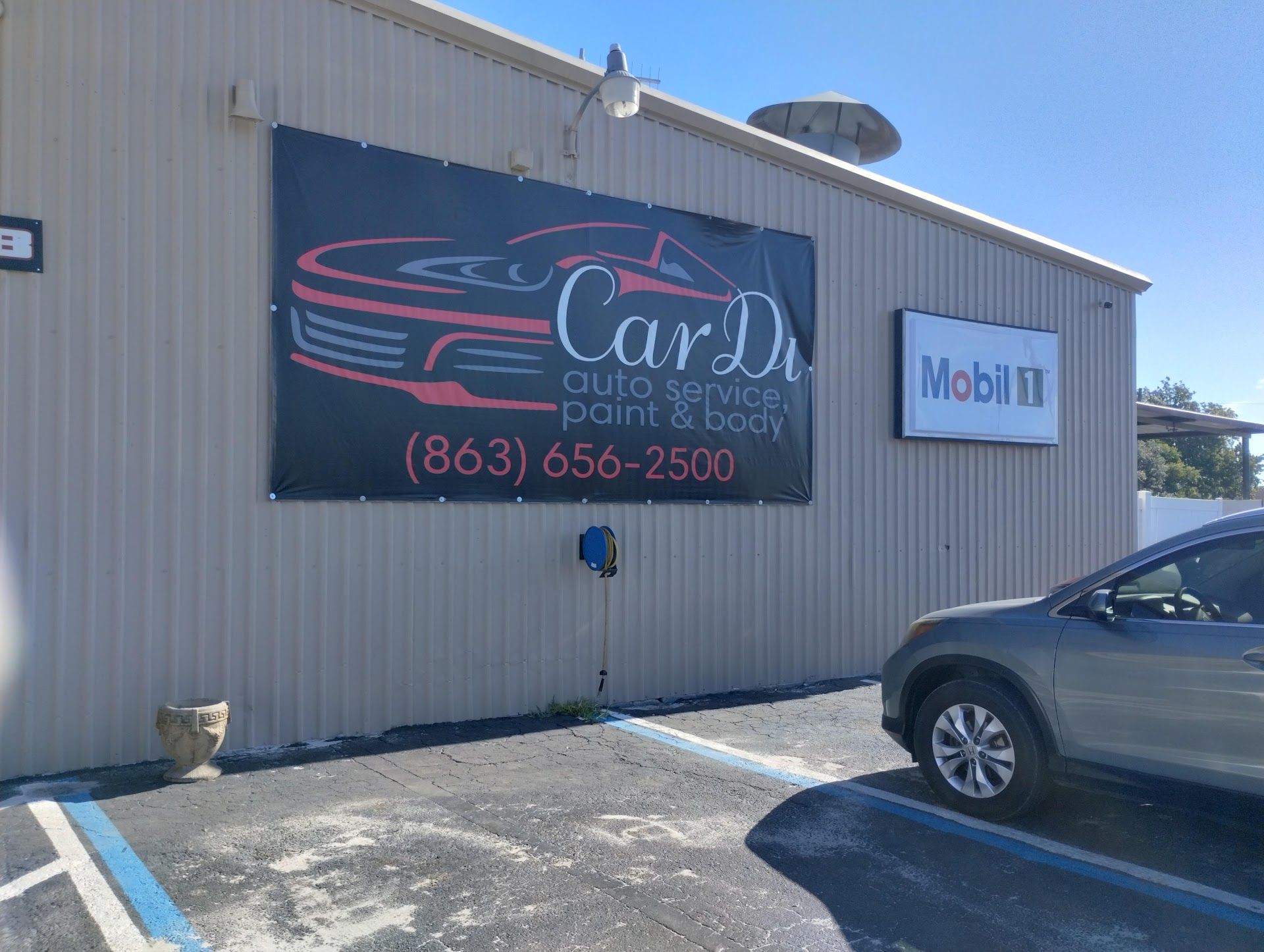 Building with large Car Dr. auto service banner and a Mobil 1 sign; parked car. | CarDi Automotive