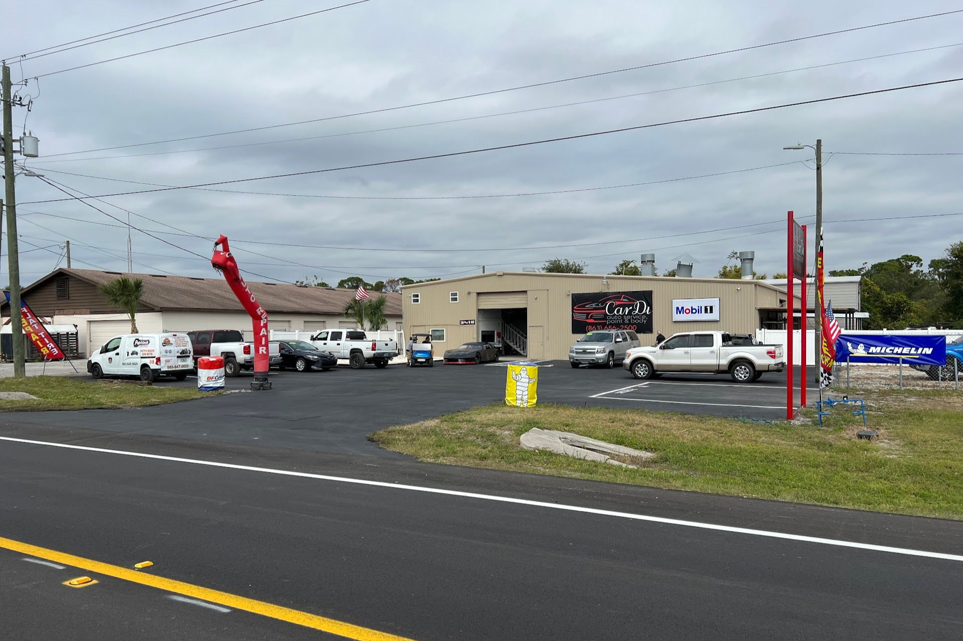 Auto repair shop with vehicles parked outside, cloudy sky overhead. Red inflatable tube man in front. | CarDi Automotive