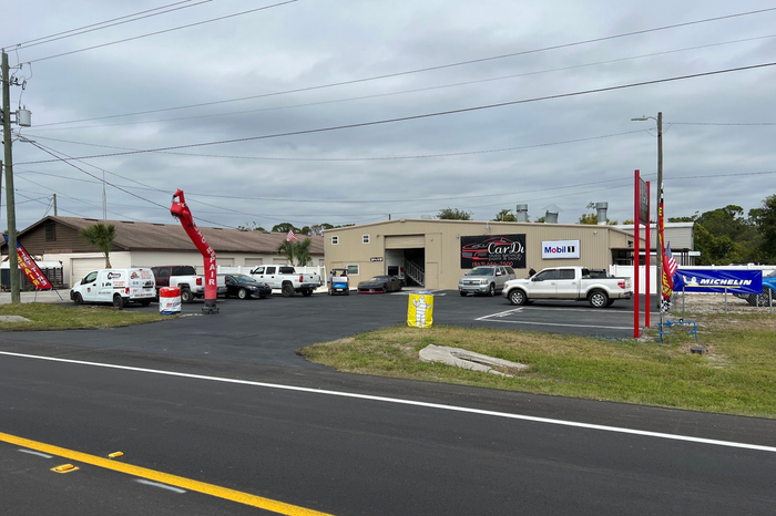 Auto repair shop with vehicles parked outside, cloudy sky overhead. Red inflatable tube man in front. | CarDi Automotive