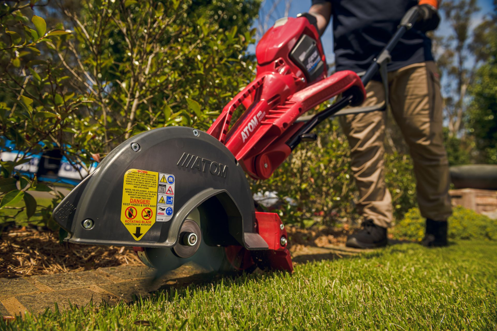 A person in tan trousers operates a red Atom edger to trim the grass along a garden bed edge— Stihl Shop Atherton In Atherton, QLD