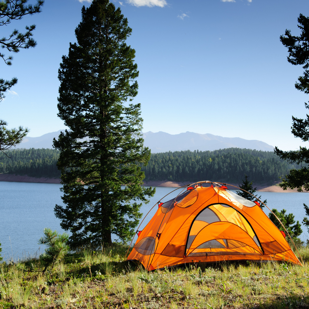 Orange tent camping near a lake with trees and grass in Johnstown Ohio