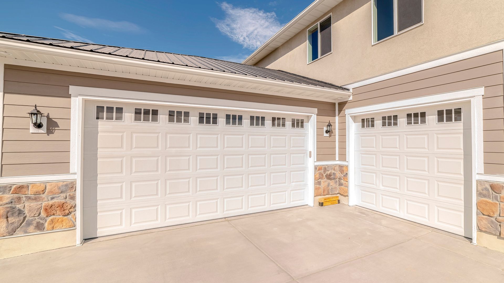 Two white garage doors on a beige house with a stone accent and a blue sky overhead.