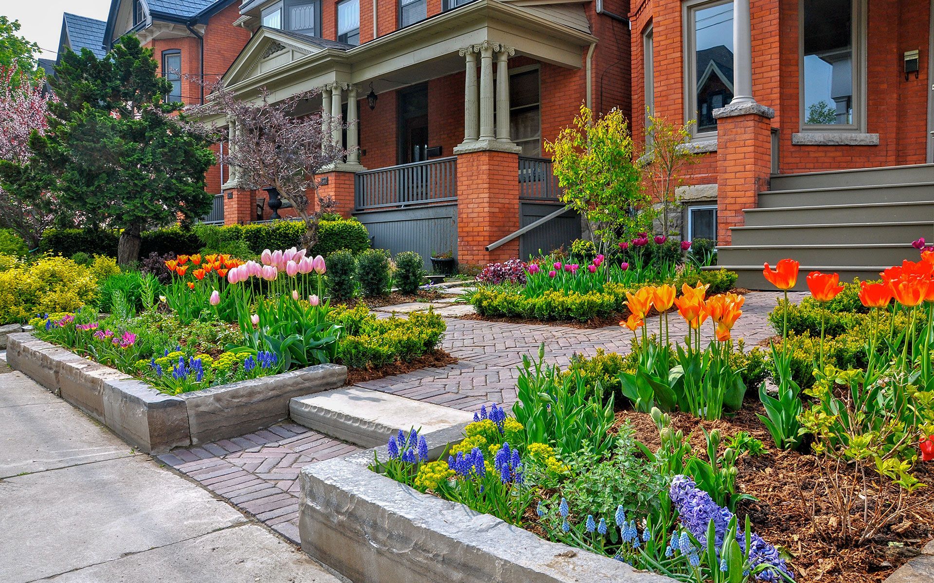 A brick house with a lush green garden in front of it.