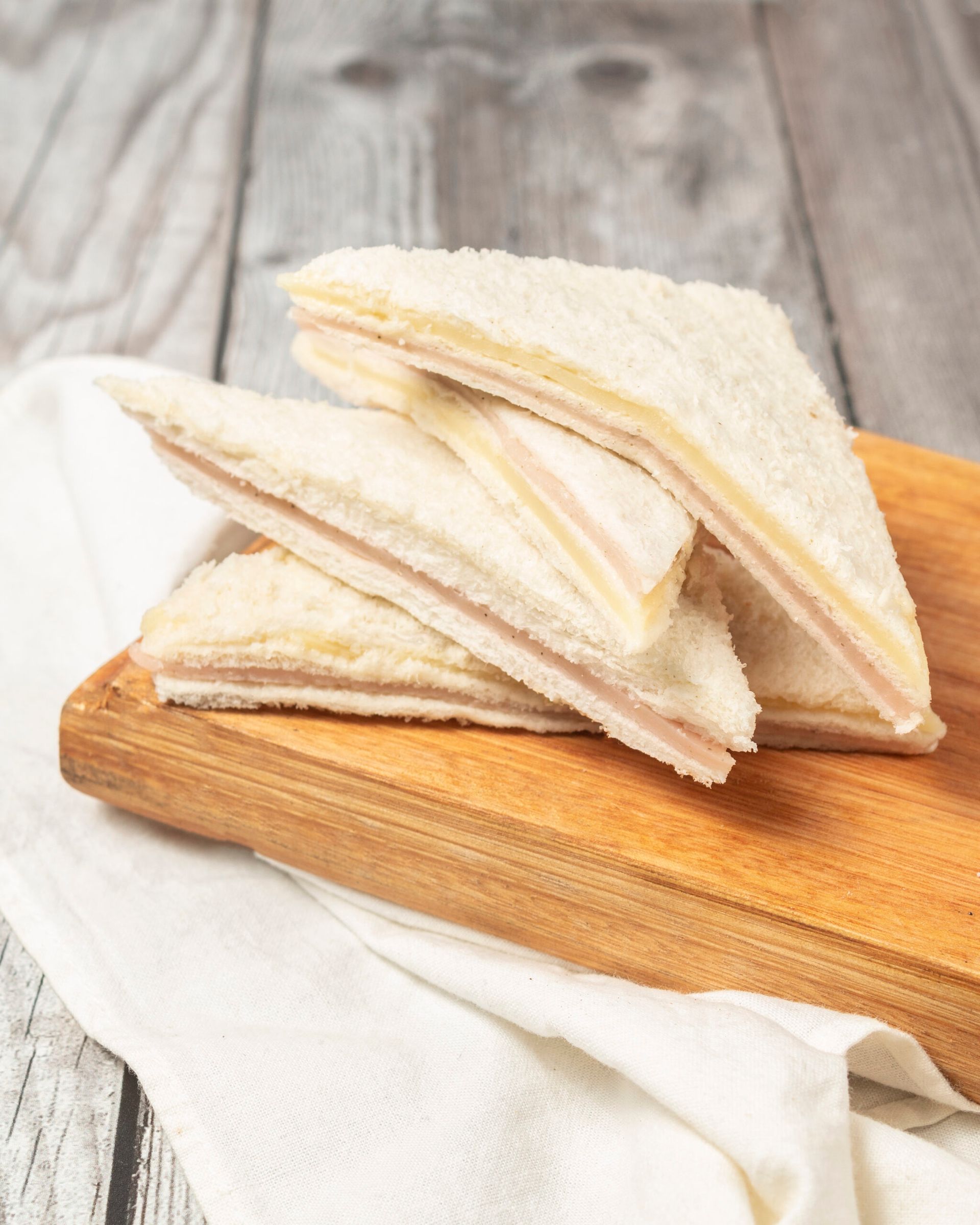 Sándwiches de jamón y queso cortados en triángulos, apilados sobre una tabla de madera