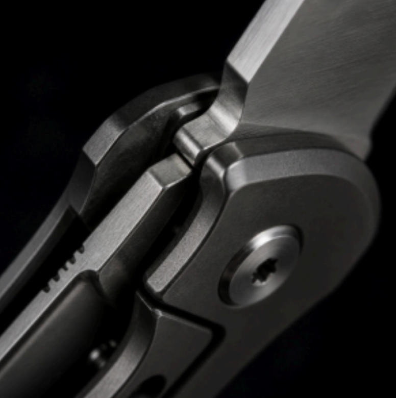 Close-up of a folding knife hinge with dark metal and brushed silver blade on a black background