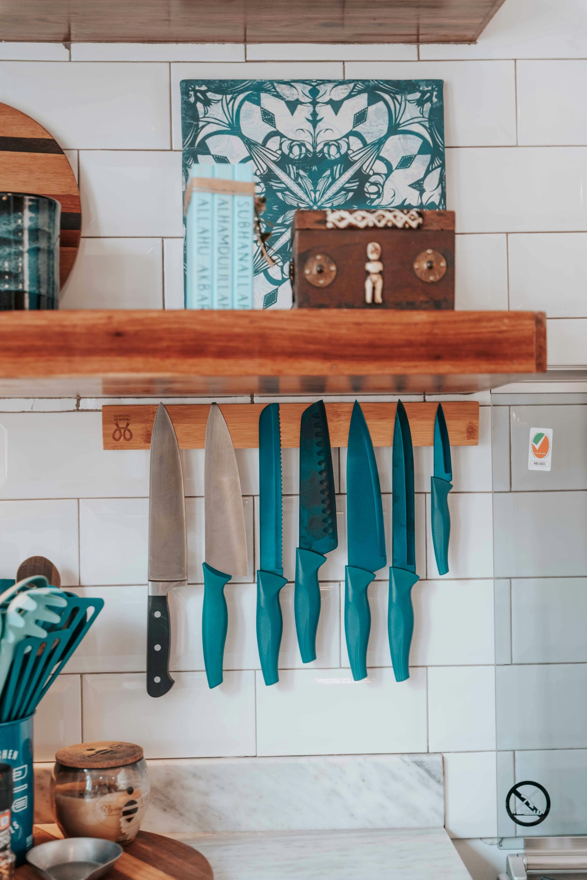 Kitchen knives hanging on a wooden rack above a countertop. White tile background with decorative items.