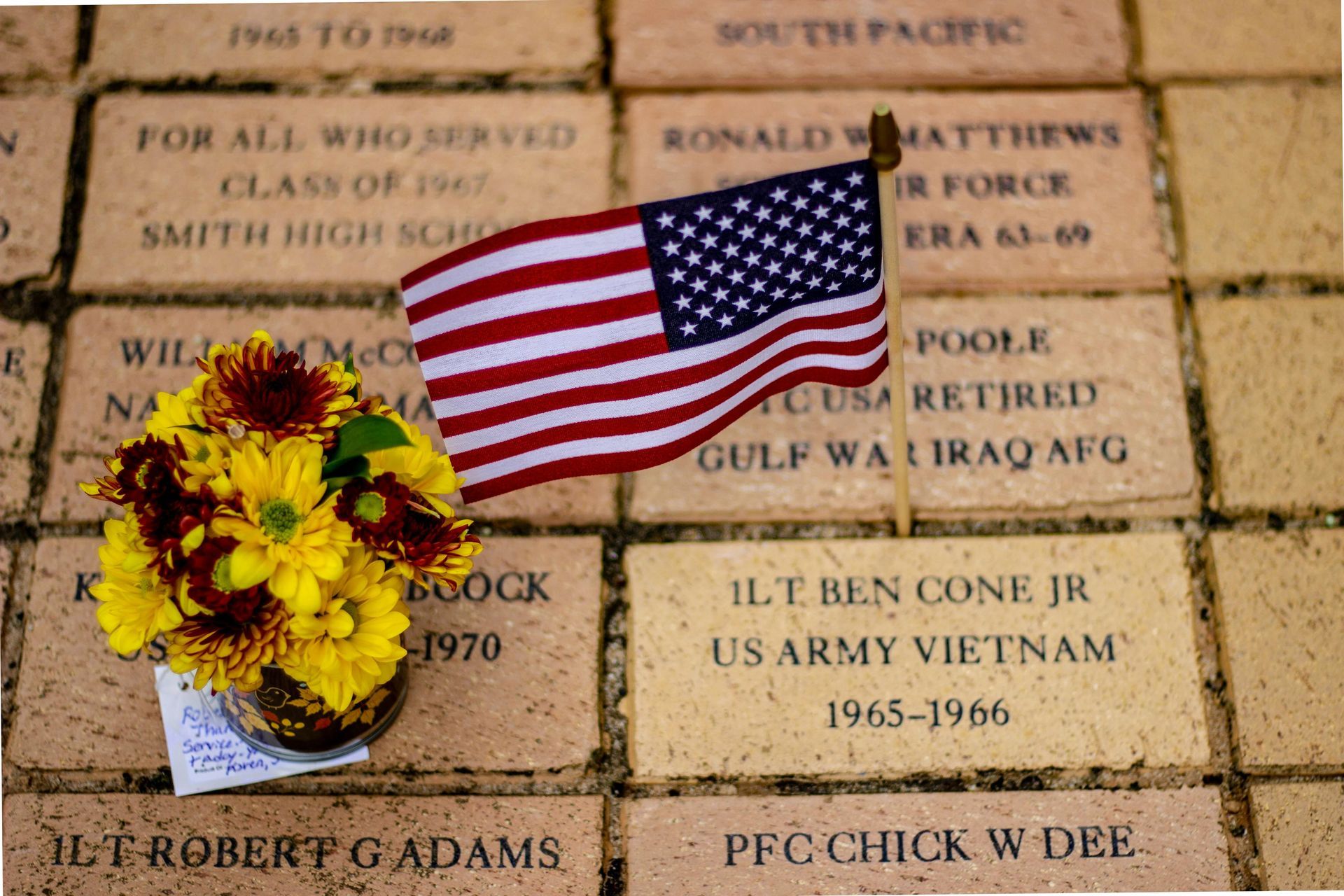 American flag and sunflowers on engraved memorial bricks at a veterans tribute site