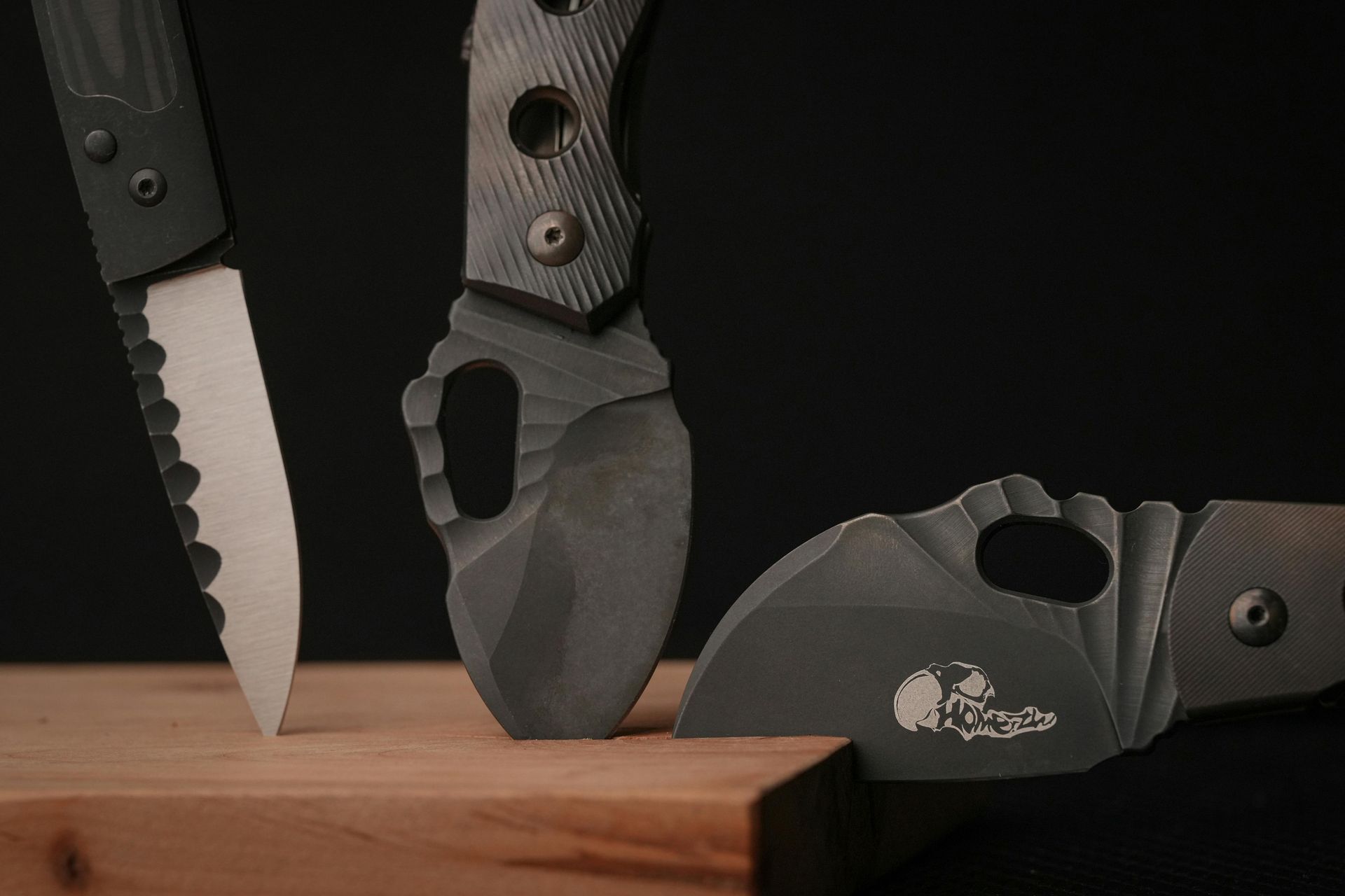 Three dark gray knives arranged on a wooden surface against a black background.