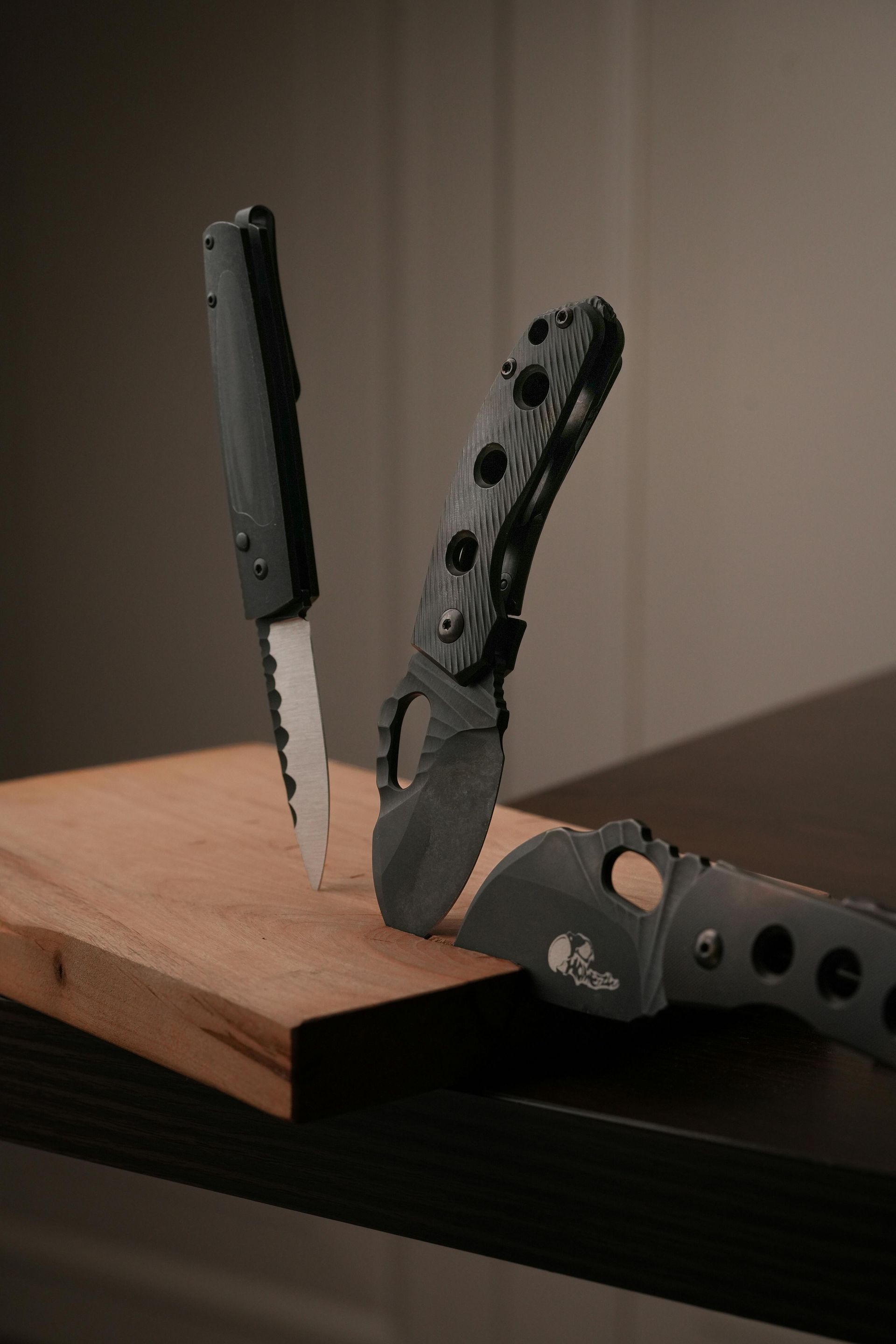 Three black knives on a wooden cutting board, one upright, two on their sides.