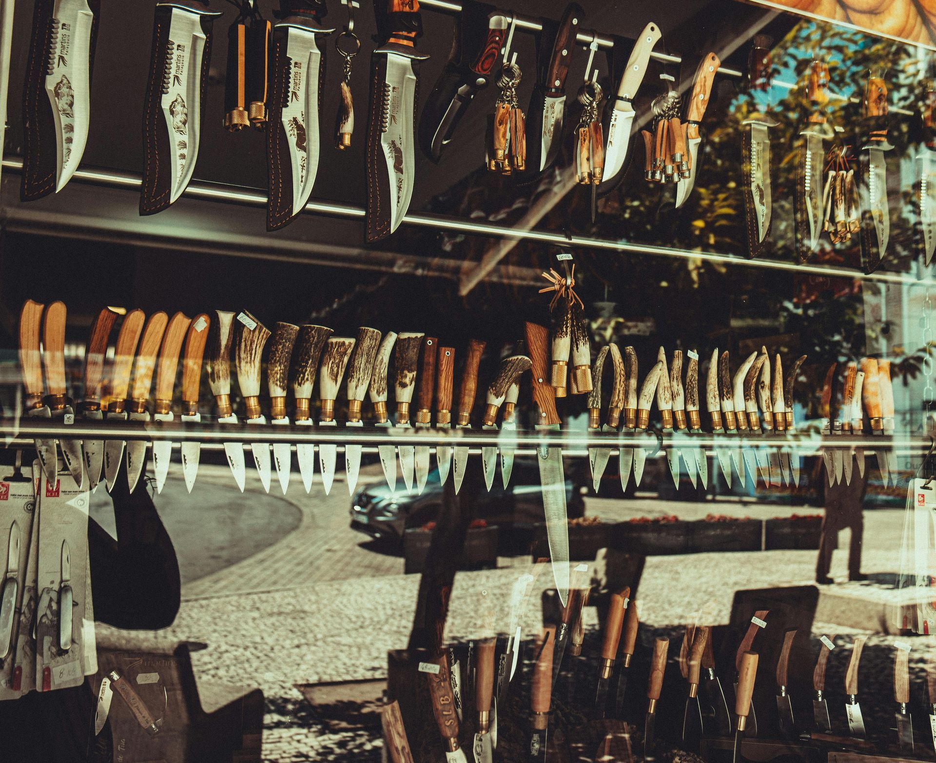 Knives displayed in a shop window, reflecting a street scene.
