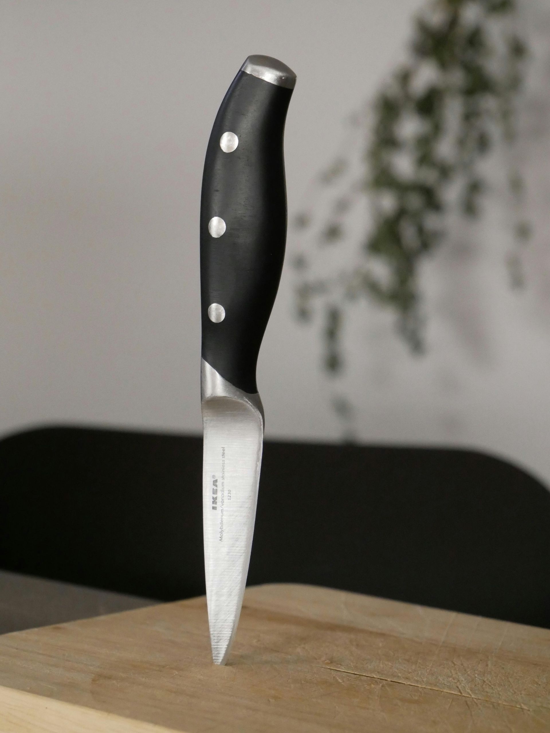 A knife is stuck in a wooden cutting board with a blurred background.