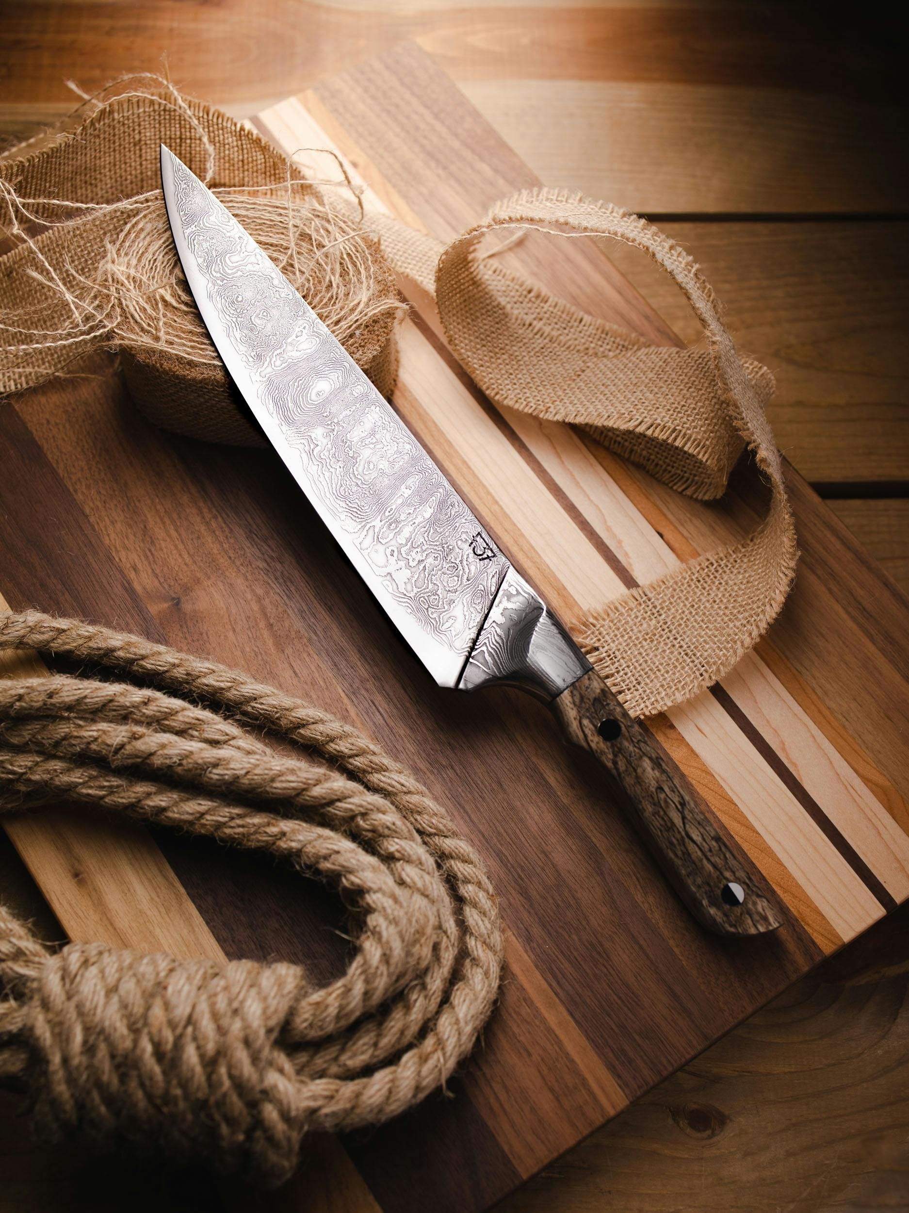 Chef's knife on a wooden cutting board with burlap and rope.