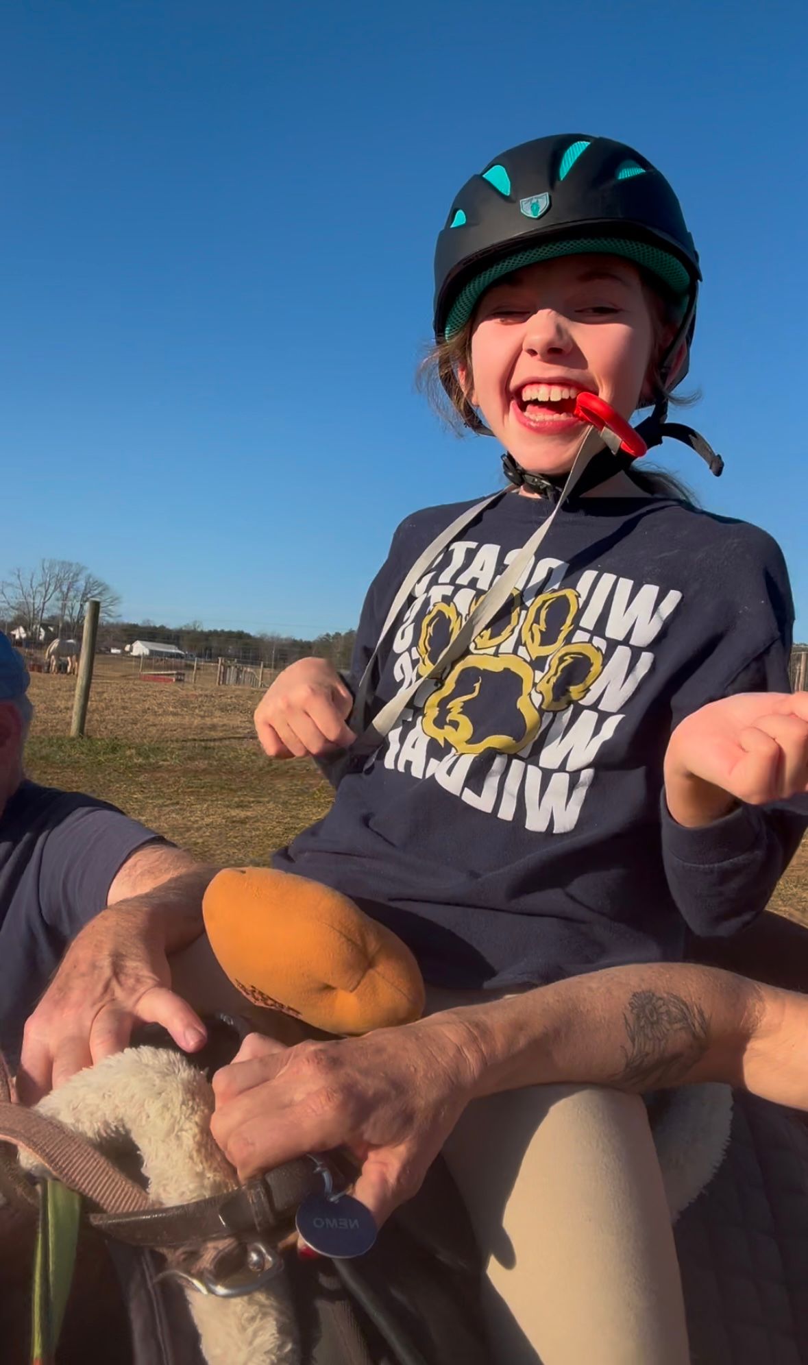 Girl riding a horse, smiling, wearing a helmet, outdoors.