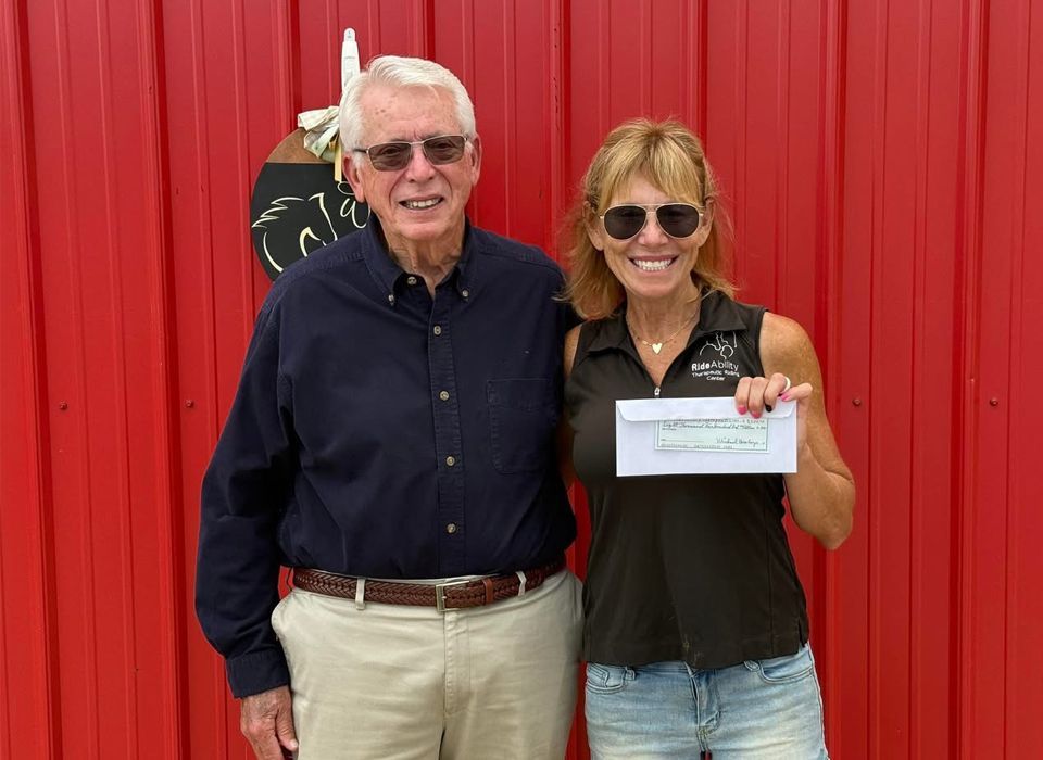 Man giving woman a check in front of a red building. Both smiling.