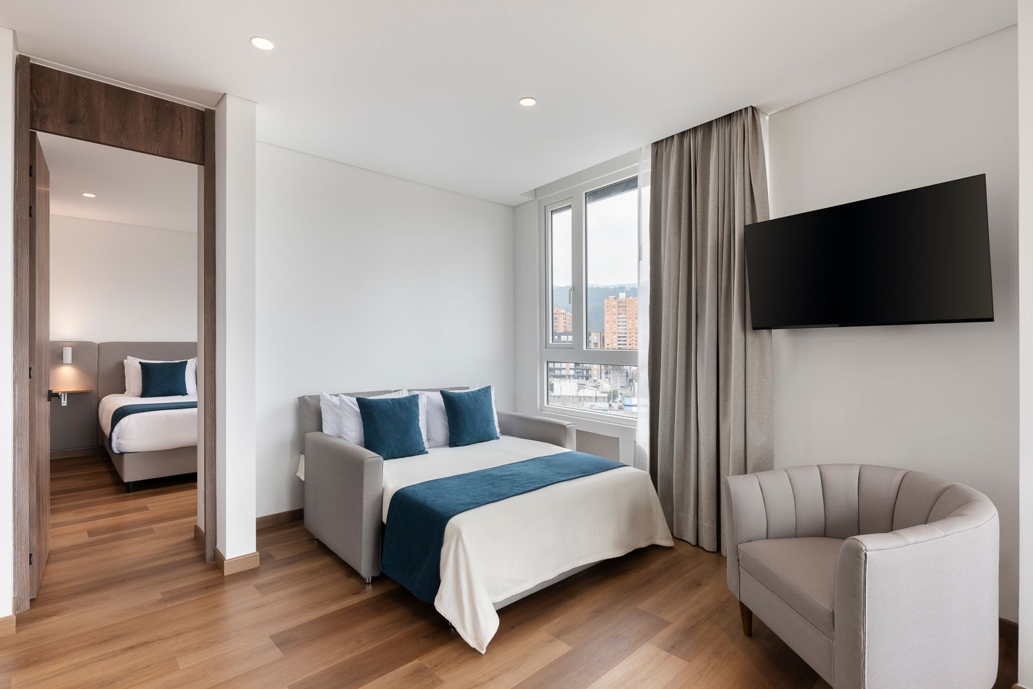 Habitación con cama doble, sala integrada y vista interior en VOU Suites, hotel en Bogotá para estadías cortas y largas.
