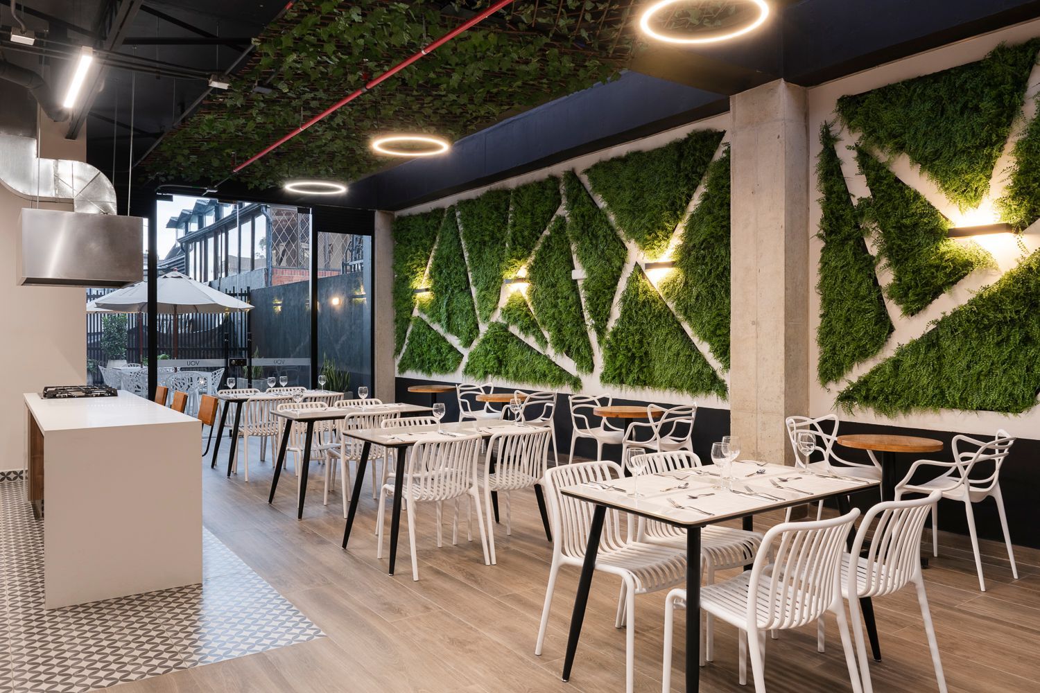 Zona de comedor con mesas, vegetación y diseño moderno en VOU Suites, hotel en Bogotá para una estadía cómoda y funcional.