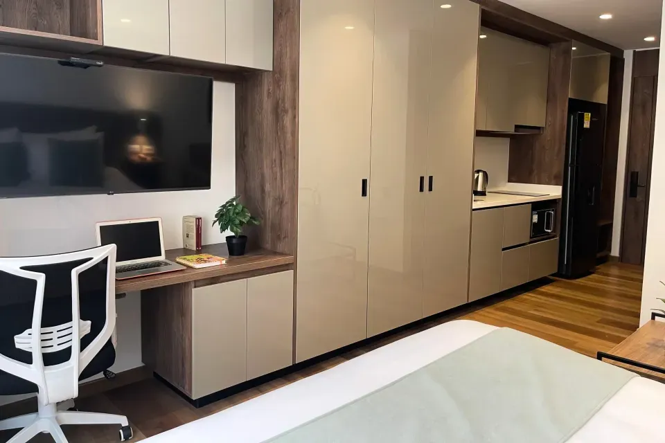 Suite tipo apartaestudio en VOU Suites Bogotá, equipada con cama doble, escritorio de trabajo con televisor de pantalla plana, cocina moderna con nevera, microondas y amplios armarios, ideal para estancias largas en Bogotá.
