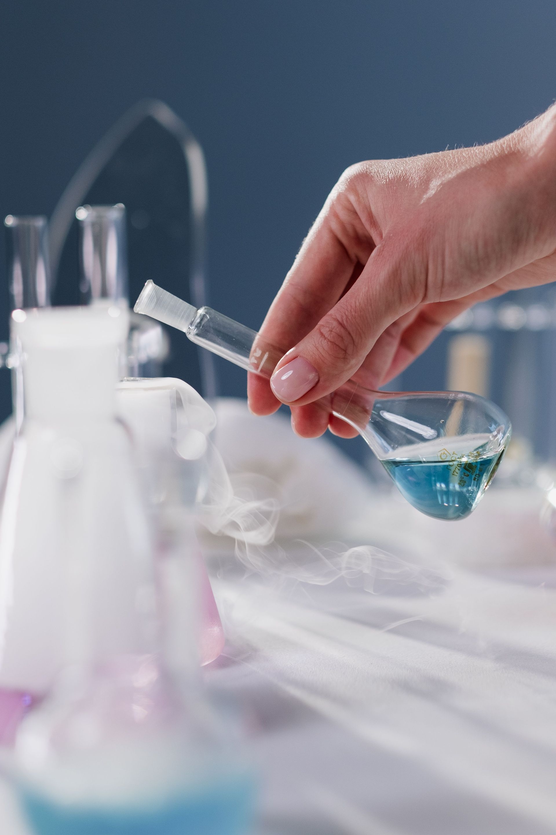 Master Senior Science Concepts with Tutorio Hand pouring blue liquid from a pipette into a small glass beaker in a lab