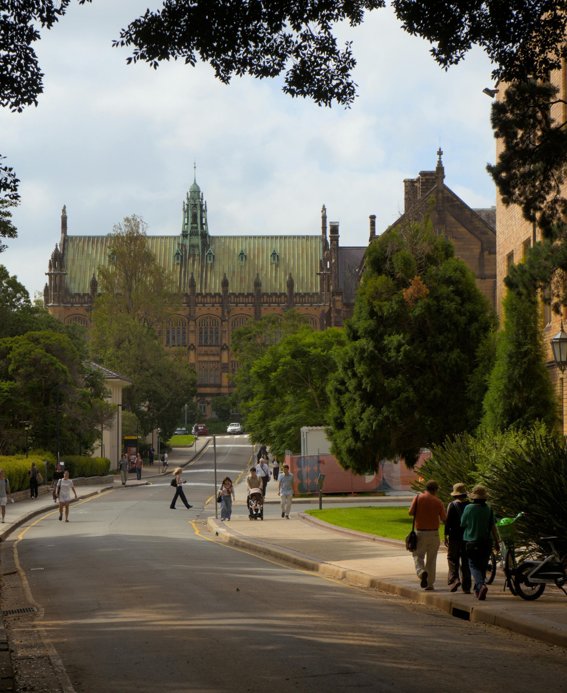 A street level view of the University of Sydney, featuring the historic Gothic-style Quadrangle building under a blue sky.