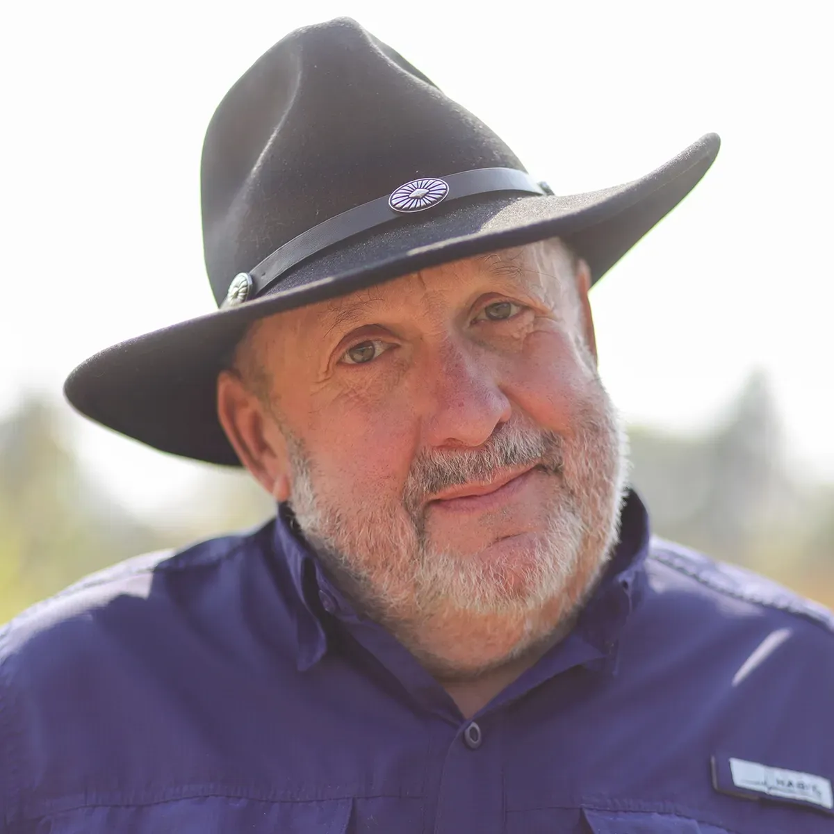 Man in black hat smiles, wearing a purple shirt outdoors.