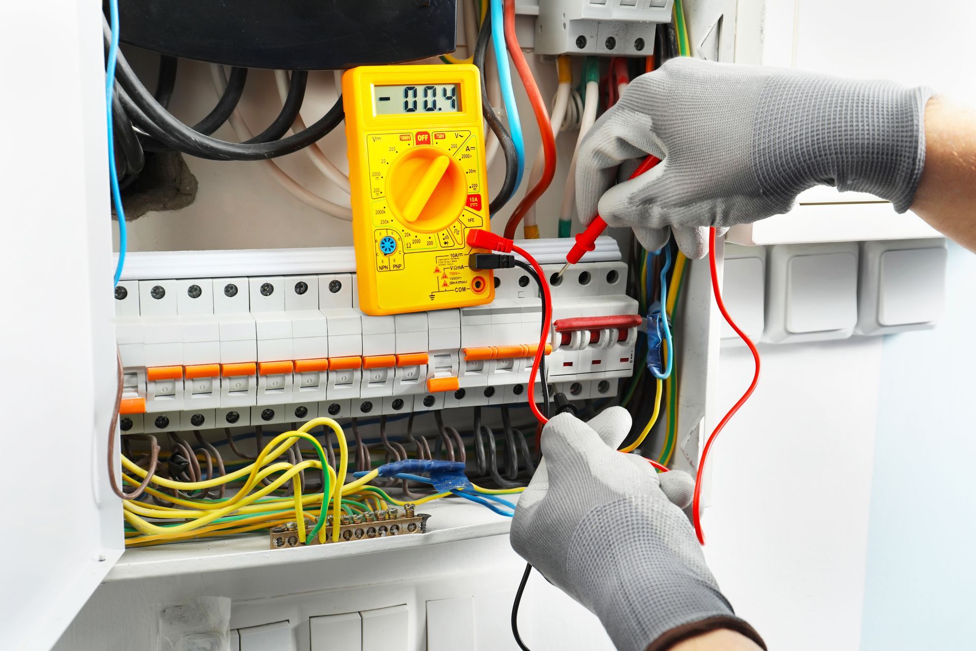 Electrician testing wires in a breaker box with a multimeter, wearing gray gloves.