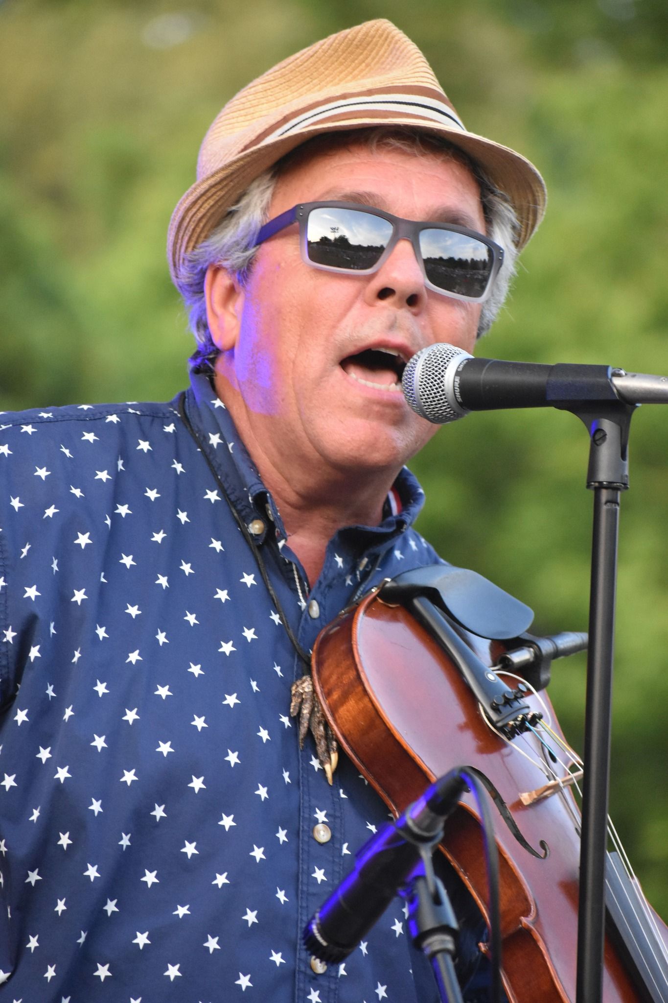 Man singing, playing a violin, wearing a straw hat and sunglasses.
