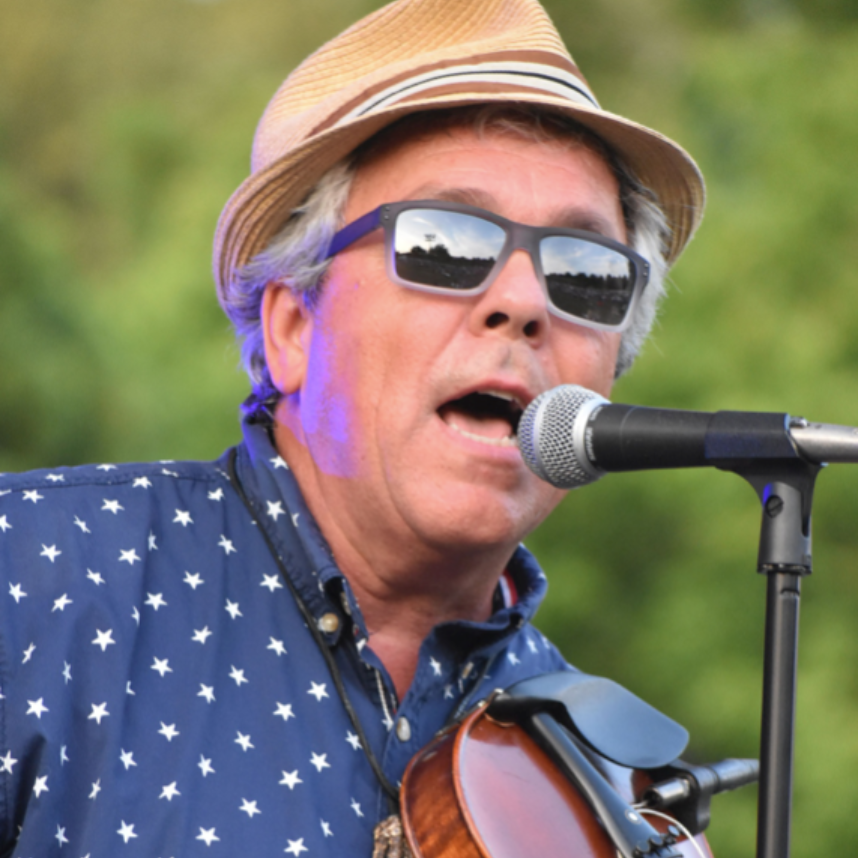 Man singing into microphone, playing violin, wearing hat, sunglasses, star-pattern shirt, outdoors.