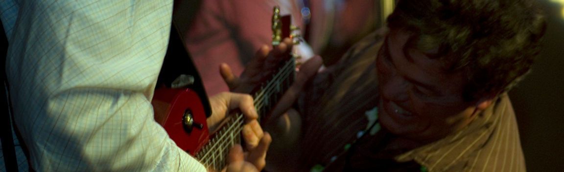 Person playing a red guitar, face of another person visible.