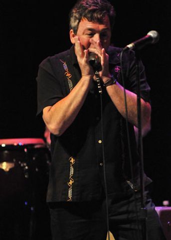 Man playing a harmonica on stage, wearing a black shirt.