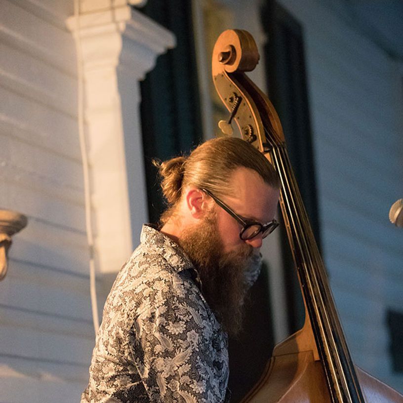 Man with beard playing upright bass outdoors at night.