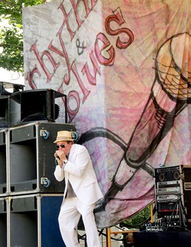 Man in white suit playing harmonica on stage in front of a 