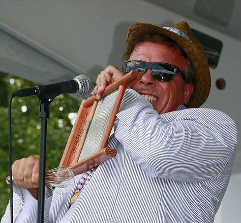 Man playing a washboard as a musical instrument, wearing sunglasses and a straw hat, outdoors.