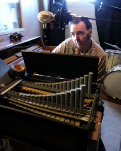 Man playing a celesta in a recording studio, microphone above.