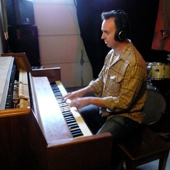 Man wearing headphones plays a vintage organ in a recording studio.