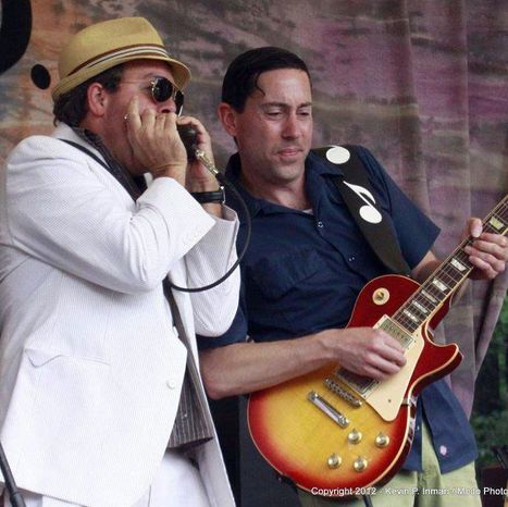 Two musicians performing blues music outdoors. One plays harmonica, the other guitar.
