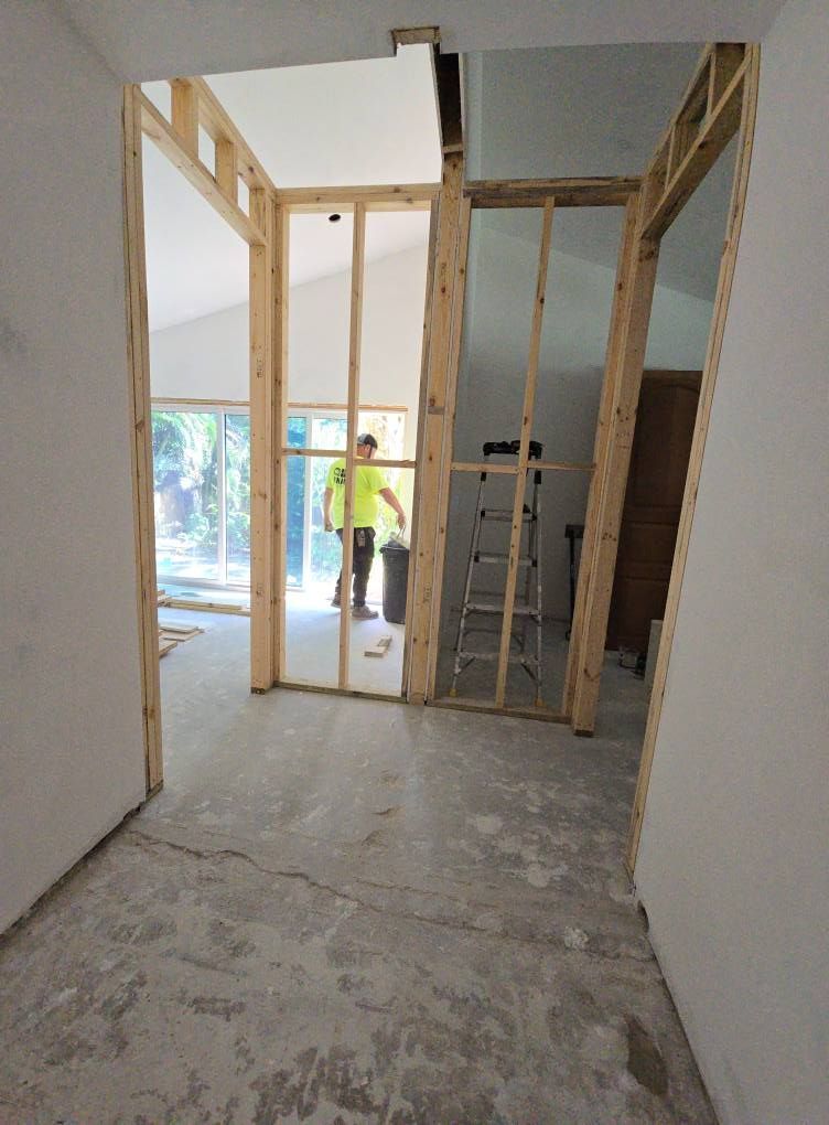 Interior hallway under construction with visible studs, worker, ladder.
