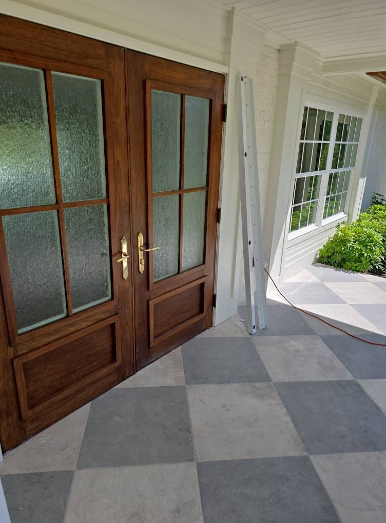 Double wooden doors with glass panes, gray and white checkered patio, a white column and window in the background.