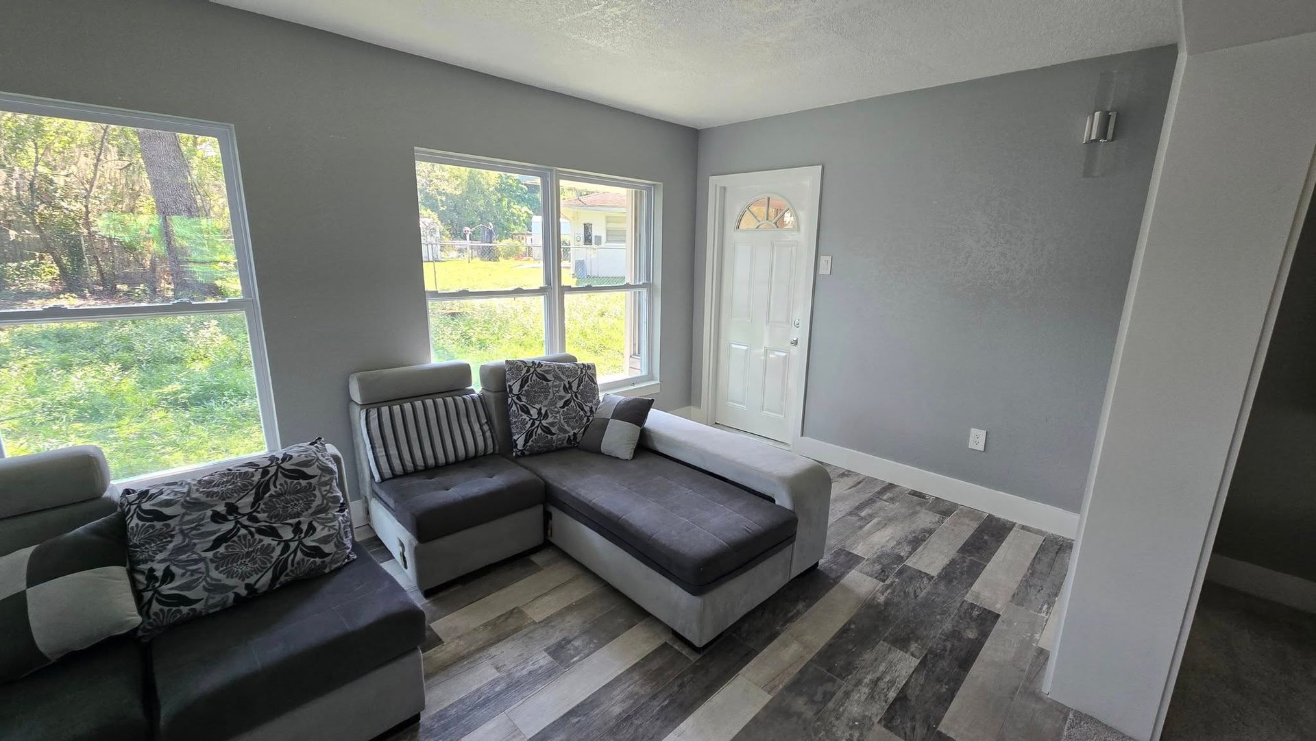 Gray living room with sectional sofa, windows, and door.