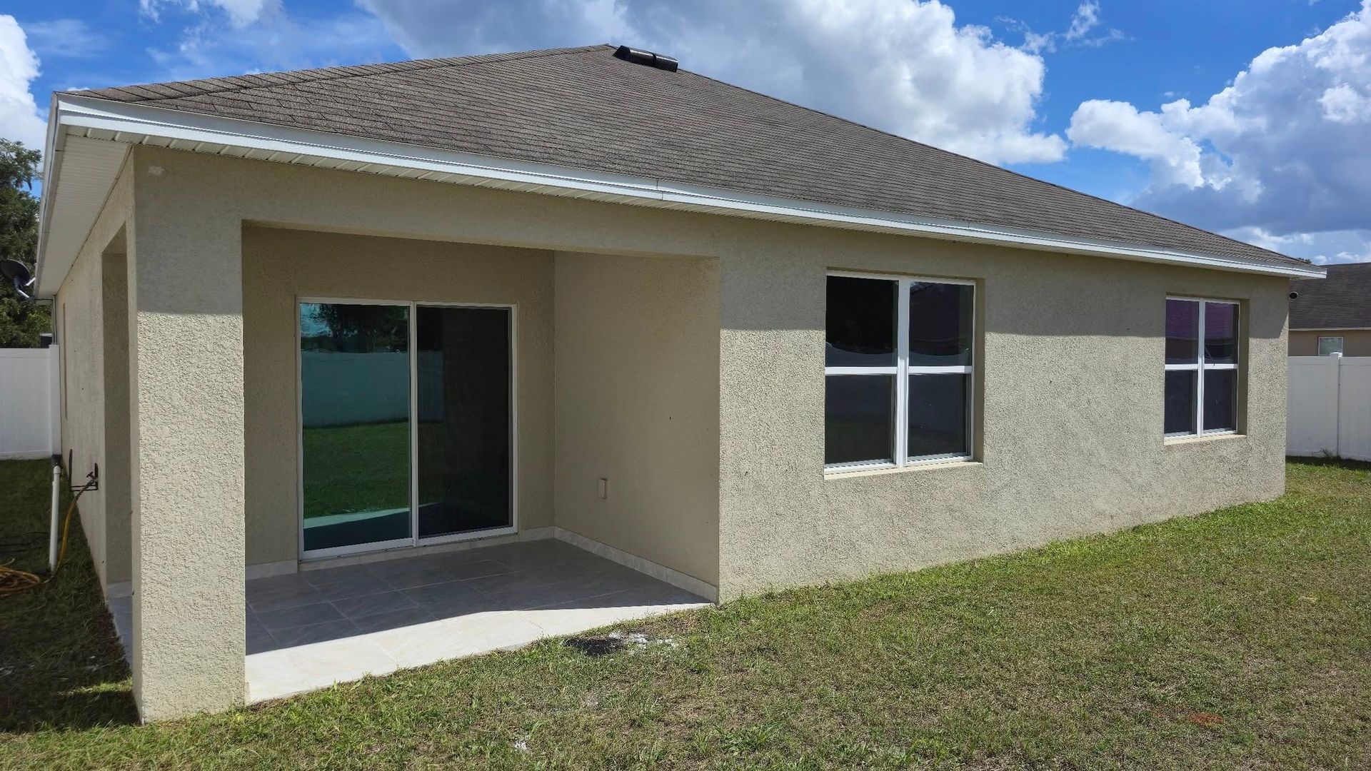 Tan stucco house exterior with covered patio, windows, and tiled roof.